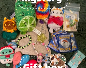 May include: A collection of items labeled Mystery Gift box including several small plush toys, a lime-shaped plush, a tie-dye plush, a white cat plush, Pokémon trading cards in a plastic bag, two beaded bracelets, two small animal figurines, and stickers.