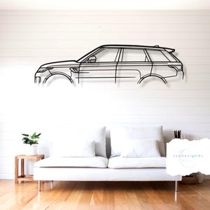 Pode incluir: Arte de parede em metal preto que retrata o perfil lateral de um carro. A obra de arte está montada numa parede branca acima de um sofá branco. O design do carro é minimalista, com linhas que definem a sua forma.