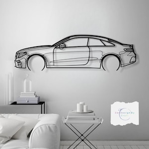May include: Black metal wall art depicting a car's side profile. The artwork features a detailed outline of the car's body, including the wheels, windows, and headlights. The car is mounted on a white wall.