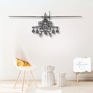 Puede incluir: Arte de pared de metal negro de un helicóptero Apache con un fondo blanco. El helicóptero está en vuelo con las aspas girando. El arte está montado en una pared blanca con una silla blanca y dos mesas auxiliares blancas en primer plano. El texto "ZenDesignByCraft" es visible en la esquina inferior derecha de la imagen.