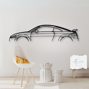 May include: Black metal wall art sculpture of a car in profile. The sculpture is mounted on a white wall. There are two white side tables and a chair with a yellow cushion in the foreground.
