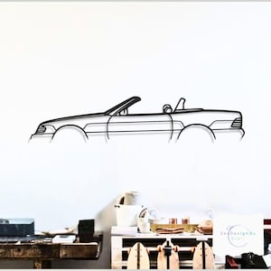 May include: Black metal wall art depicting a convertible car. The artwork is a minimalist outline of the vehicle, showcasing the car's profile with its top down. The design is mounted on a white wall, creating a striking contrast.