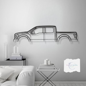 May include: Black metal wall art depicting the outline of a pickup truck. The art is displayed on a white wall in a living room setting with a white sofa and a small table with candles.