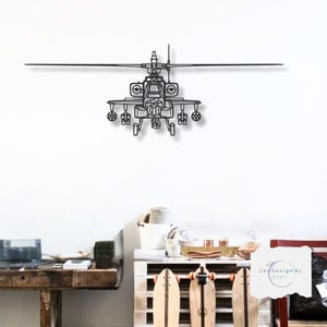 May include: A black and white line drawing of an Apache helicopter on a white wall. The helicopter is facing the viewer and has a detailed design. The image is in a room with a wooden table and a shelf with skateboards.