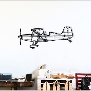 May include: Black metal airplane wall art. The biplane design features a propeller, wings, and tail, with a detailed wireframe construction. The artwork is mounted on a white wall, adding a touch of aviation-themed decor to any space.