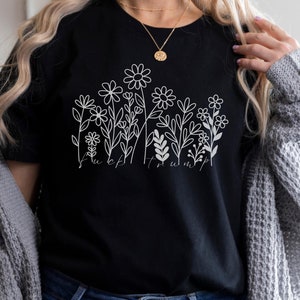 May include: Black t-shirt with a white floral design and the text "F*ck Trump". The graphic features various flower and leaf illustrations. The shirt is made of a soft material.