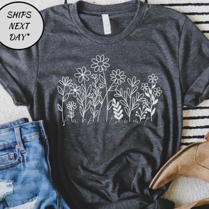 May include: Dark gray t-shirt with a white floral design and the text "fuck trump". The shirt is paired with denim shorts and tan boots. The image is on a striped rug.