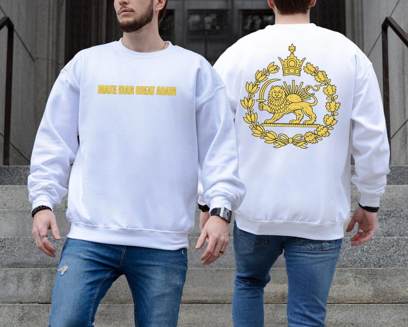 May include: White sweatshirt with the text "MAKE IRAN GREAT AGAIN" in gold lettering on the front. The back features a gold emblem with a lion, crown, and wreath design. The sweatshirt is paired with blue jeans.