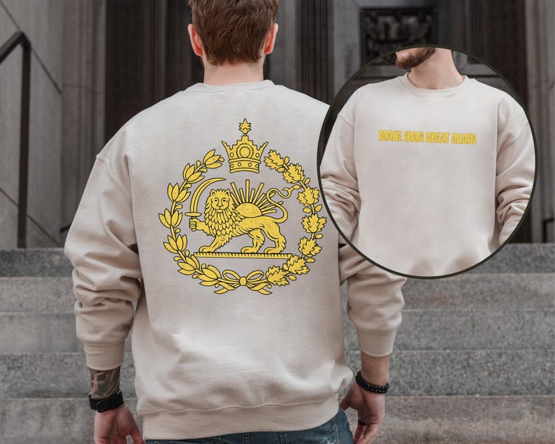 May include: Beige sweatshirt featuring a yellow emblem of a lion holding a sword, a crown, and a wreath. The back of the sweatshirt has the text "MAKE THE GREAT AGAIN" in yellow. The sweatshirt is made of a soft material.