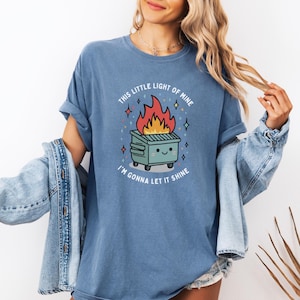 May include: A blue t-shirt with a graphic of a burning dumpster with a smiling face and the text "This little light of mine I'm gonna let it shine".