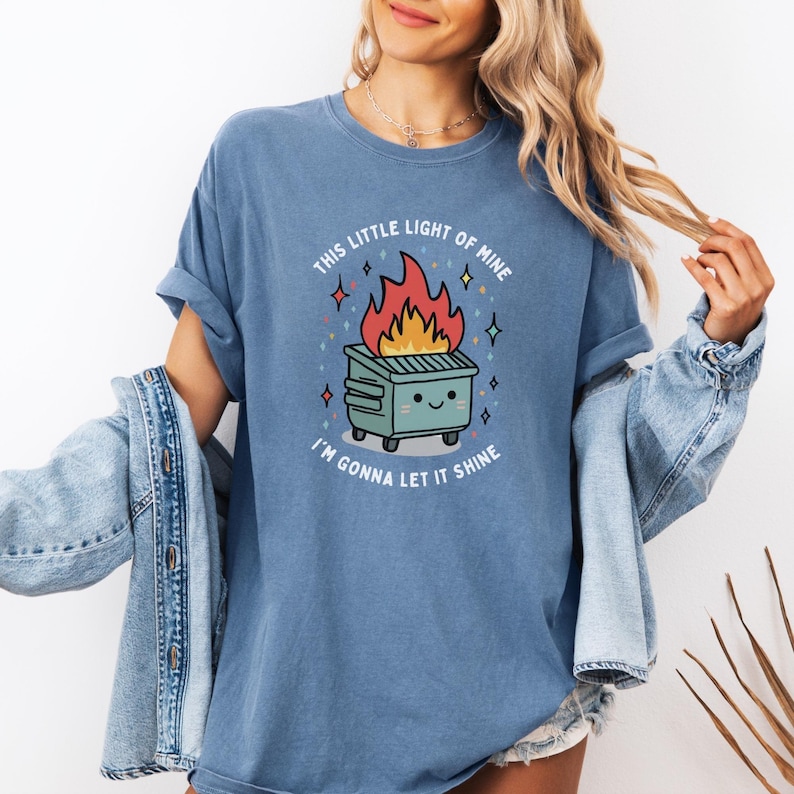 May include: A blue t-shirt with a graphic of a burning dumpster with a smiling face and the text "This little light of mine I'm gonna let it shine".