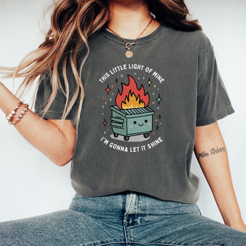 May include: A gray t-shirt with a graphic of a burning trash can with a smiling face and the text "This little light of mine, I'm gonna let it shine."