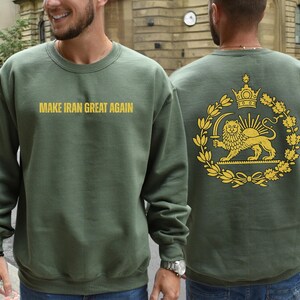 May include: Olive green sweatshirt with the text "MAKE IRAN GREAT AGAIN" in gold lettering on the front. The back features a gold emblem with a lion, crown, and sun design. The sweatshirt is a crew neck style.