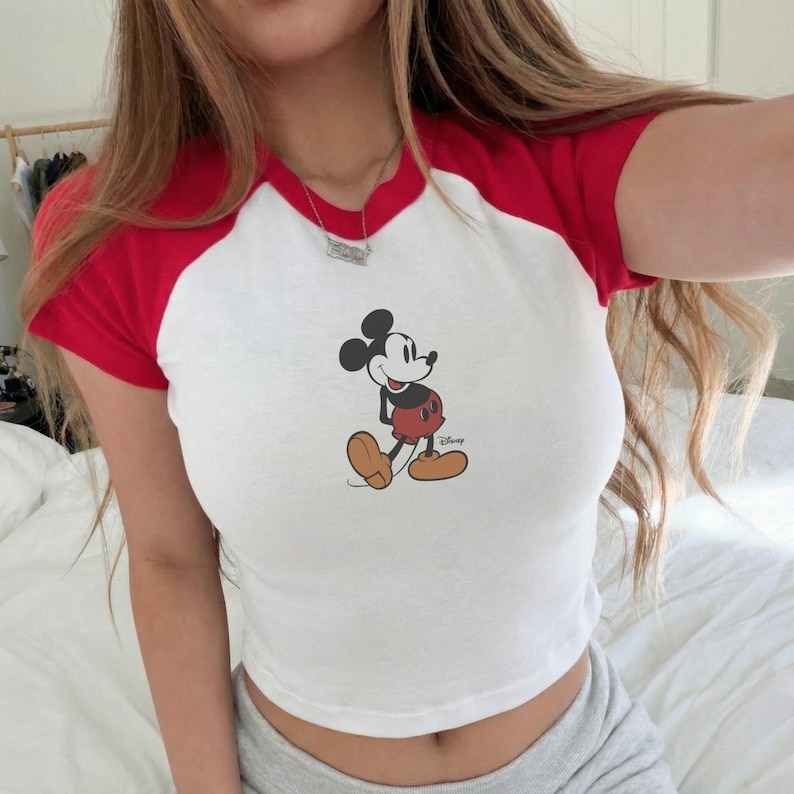 Op de afbeelding: Witte crop top met rode korte mouwen en kraag met een Mickey Mouse-afbeelding. Het Disney-shirt heeft een casual, retro stijl. De top is gemaakt van een zacht materiaal.