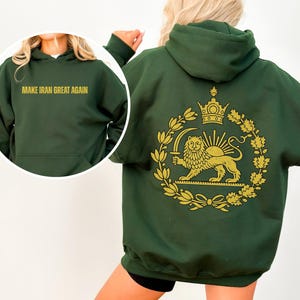 May include: Dark green hoodie with the text "MAKE IRAN GREAT AGAIN" in gold lettering on the front. The back features a gold emblem with a lion, crown, and sun design. The hoodie has a hood and a front pocket.