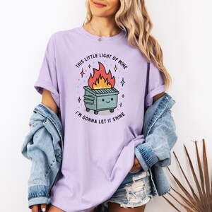 May include: A purple t-shirt with a graphic of a cartoon trash can on fire with the text "This little light of mine, I'm gonna let it shine."