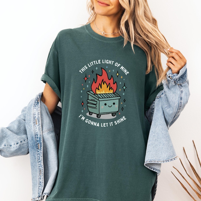 May include: A teal green t-shirt with a cartoon image of a dumpster on fire with the text "This little light of mine, I'm gonna let it shine."