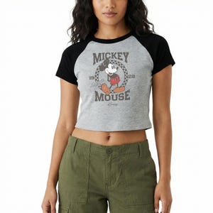 May include: A gray crop top with black sleeves featuring a vintage Mickey Mouse graphic. The graphic includes the words "Mickey Mouse" and the years "1928" and "1928". The shirt is made of a soft material.