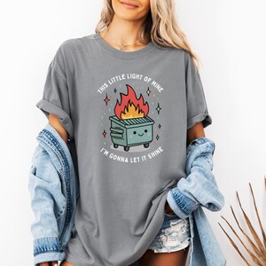 May include: Gray t-shirt with a graphic of a cartoon dumpster on fire with the text "This little light of mine I'm gonna let it shine".