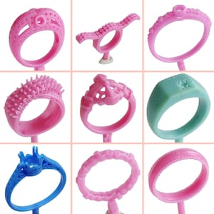 Può includere: Nove stampi per anelli in cera rosa e blu per la creazione di gioielli. Gli stampi sono in vari stili, tra cui un anello con una corona, un anello con una fascia testurizzata e un anello con una fascia semplice.