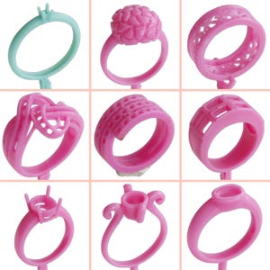 May include: Nine different wax ring designs for jewelry making. The rings are made of pink and light blue wax and are displayed on a white background.