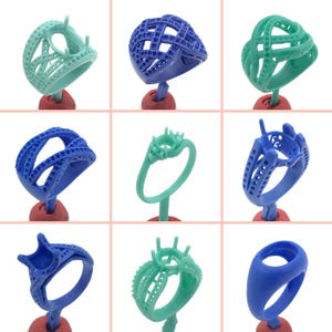 May include: Nine different 3D printed wax ring models in blue and green. The rings are displayed on small red stands.