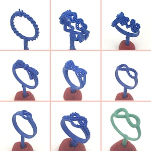 May include: Nine different wax ring designs for jewelry making. The rings are displayed on small red stands. The rings are all blue except for one which is green.