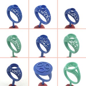 Puede incluir: Un conjunto de nueve anillos de cera azules y verdes con diseños intrincados. Los anillos se muestran en pequeños soportes.