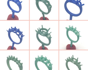 May include: Nine wax ring settings for jewelry making. Three are blue and six are green. The rings are on small red stands.