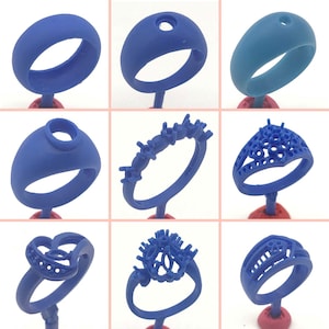 Könnte beinhalten: Neun verschiedene blaue Wachsringformen für die Schmuckherstellung. Die Formen werden auf roten Ständern ausgestellt. Einige der Formen haben komplizierte Designs, während andere einfache Bänder sind.