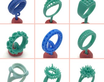 May include: Nine different wax ring designs for jewelry making. The rings are made of blue and green wax and are displayed on red bases.
