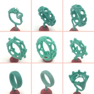 May include: A collection of nine turquoise-colored wax ring molds, each mounted on a red base. The designs vary, showcasing intricate patterns and shapes, including open circles and detailed settings, ready for the jewelry-making process.