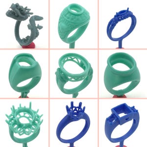 May include: Nine different wax ring designs for jewelry making. The rings are made of a light green and blue wax. The rings are displayed on small stands.