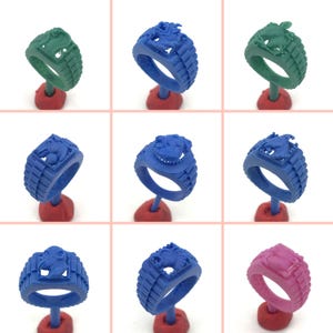 May include: Nine wax rings with different animal designs. The rings are in various colors, including green, blue, and pink. The rings are displayed on small stands.