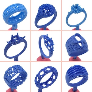 Pode incluir: Nove moldes de anel de plástico azul para a fabricação de joias. Os moldes estão em pequenos suportes cor-de-rosa. Os moldes são de diferentes designs, alguns com detalhes intrincados.