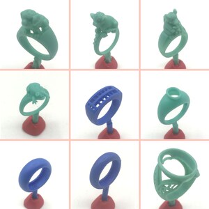 May include: Nine different wax ring designs for jewelry making. The rings are displayed on red stands and are made of green and blue wax.
