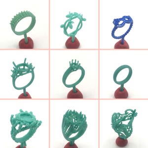 May include: Nine different wax ring designs for jewelry making. The rings are displayed on red stands and are made of a light green wax.