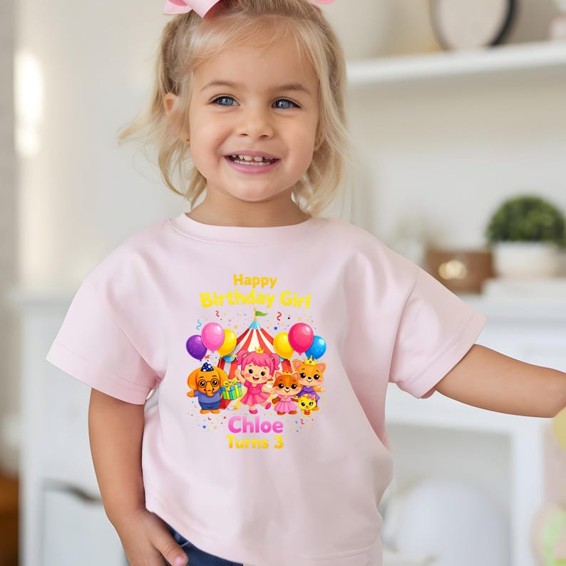 Op de afbeelding: Lichtroze T-shirt met een kleurrijke afbeelding. De afbeelding bevat de tekst "Happy Birthday Girl", de naam "Chloe" en het nummer "3". De afbeelding toont cartoonfiguren, ballonnen en een circustent.