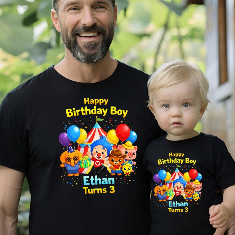 Op de afbeelding: Zwarte T-shirts met een kleurrijke afbeelding van cartoonfiguren, ballonnen en een circustent. De tekst op de shirts luidt "Happy Birthday Boy" en "Ethan Turns 3".