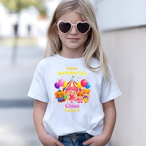 Op de afbeelding: Wit T-shirt met een kleurrijk verjaardagsontwerp. De afbeelding bevat de tekst "Happy Birthday Girl Chloe Turns 3", cartoonfiguren, ballonnen en een circustent.