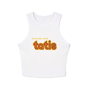 以下が含まれることがあります： オレンジと黄色の文字で「SHOW ME YOUR tatis」と書かれた、白いノースリーブのクロップトップです。