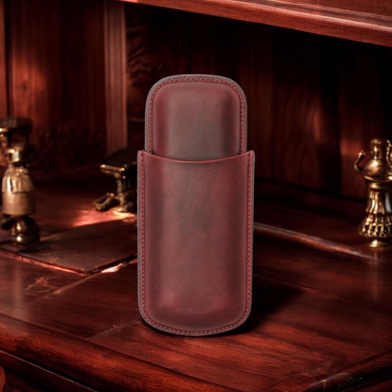 May include: A burgundy leather cigar case with a flap closure. The case is made of high-quality leather and has a smooth finish.