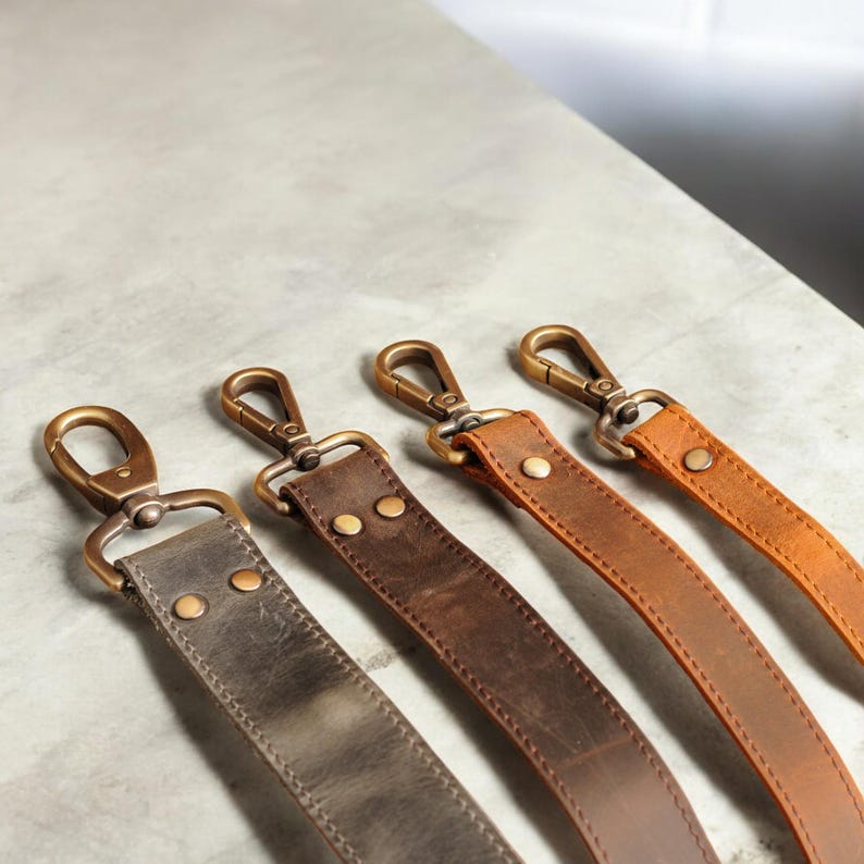 May include: Four leather straps with brass clasps. The straps are in different shades of brown, including gray, dark brown, and light brown.