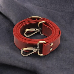 May include: A red leather strap with two brass clasps. The strap is rolled up and the clasps are visible.