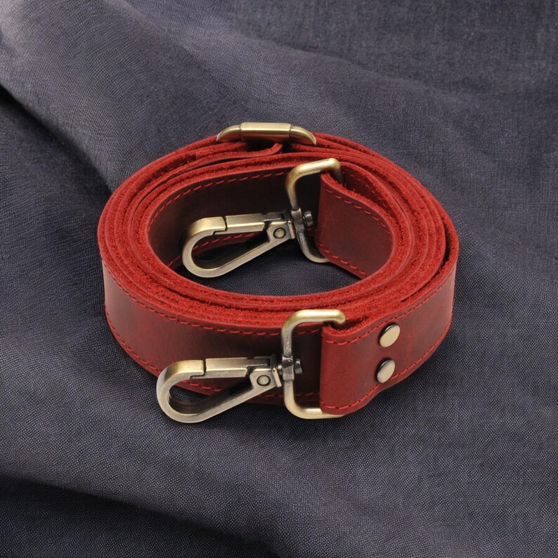May include: A red leather strap with two brass clasps. The strap is rolled up and the clasps are visible.