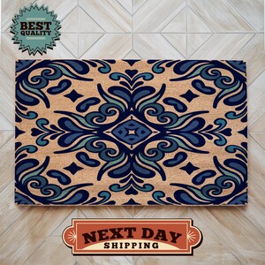 May include: A rectangular doormat with a beige background and a symmetrical design in shades of blue and teal. The design features floral and geometric elements. The words "BEST QUALITY" are in a teal badge. The words "NEXT DAY SHIPPING" are in a brown badge.