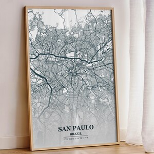 May include: A framed map print of San Paulo, Brazil, in shades of gray and teal. The city map is detailed with streets and landmarks. The print includes the city name, country, and coordinates. The frame is a light wood color.