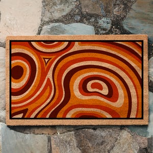 May include: A brown coir doormat with a geometric pattern of orange, red, and brown swirls. The pattern resembles a retro 70s design.