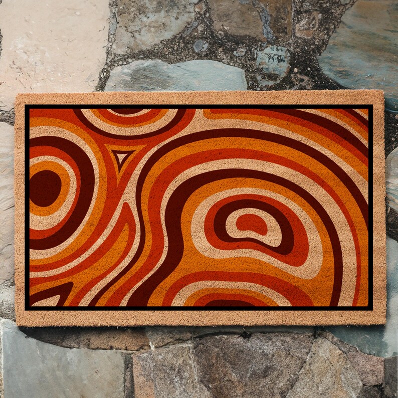 May include: A brown coir doormat with a geometric pattern of orange, red, and brown swirls. The pattern resembles a retro 70s design.