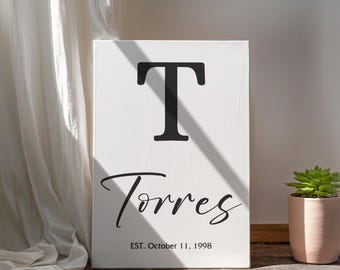 May include: White canvas sign with a black letter "T" and the text "Torres" in cursive script. Below the name is the text "EST. October 11, 1998".